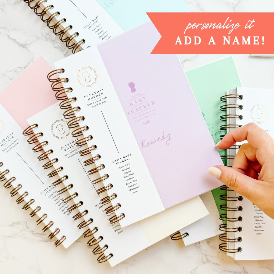 Assortment of spiral-bound Daily Baby Tracker planners from The Everyday Mother spread out, with one open to a page that offers a personalization option where you can add a name.