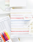 Overhead shot of the contents of The Everyday Mother 'Bundle of Joy' gift set spread out, including a baby tracking journal, colorful pens, thank you cards, and tracking sheets. All items are elegantly arranged on a white background, showing the thoughtful and comprehensive nature of this baby journal kit.