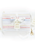Elegant presentation of The Everyday Mother 'Bundle of Joy' baby journal gift set, featuring a striped journal case tied with a white satin ribbon and a tag. This set includes a golden pen and a neatly organized package, highlighting the thoughtful and practical design for new parents to track their baby's growth and milestones.