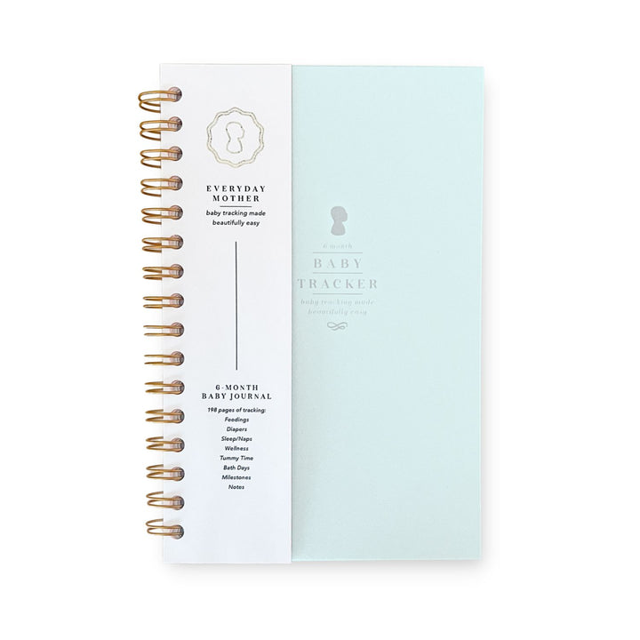 A Daily Baby Tracker journal by The Everyday Mother, with a spiral binding, featuring sections for daily nursing log, diapering, sleeping, and baby care notes.