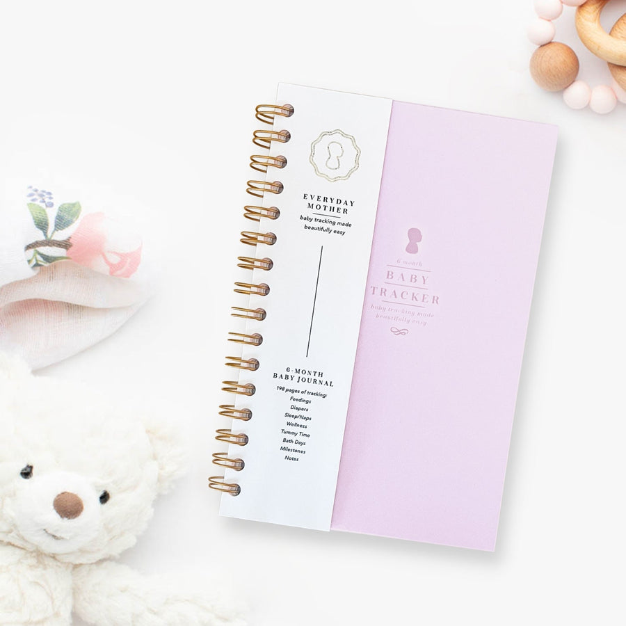 A closed purple lilac Everyday Mother Baby Tracker book showing the ivory cover, white cover slip with gold logo, and gold spiral rings